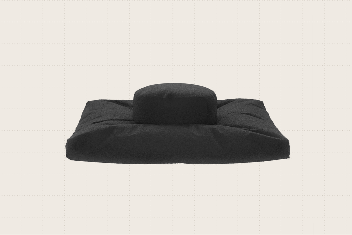 A bouclé meditation pillow shown in black. It's a flat, rectangular cushion with another raised, round cushion in the center.