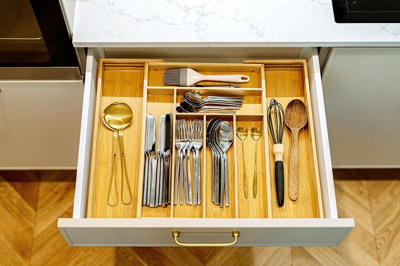 An expandable bamboo organizer inside a kitchen's cutlery drawer.