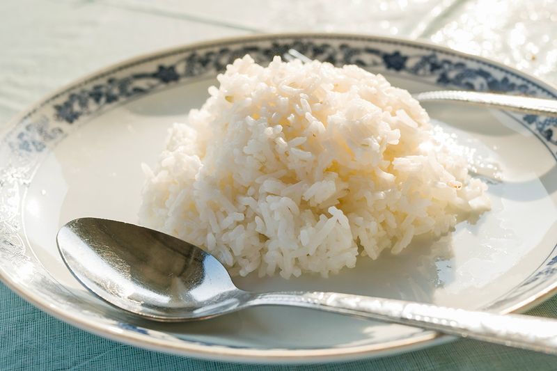 A plate with a blue floral motif around the rim with a scoop of white rice in the center. Next to it on the plate is a silver spoon.