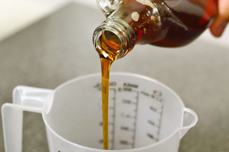 Anonymous person pouring maple syrup into a plastic measuring container.