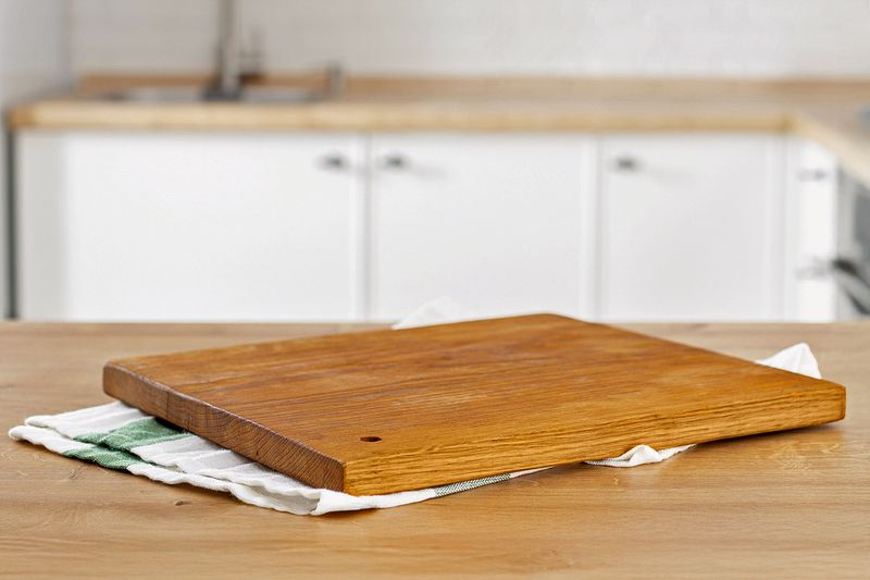 A wooden cutting board placed on top of a kitchen towel on a butcher block kitchen countertop.