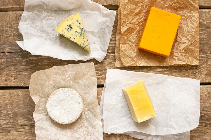 Four different types of cheeses on wrapping paper. It's shot from above and the wrappers are on a slatted wood table.