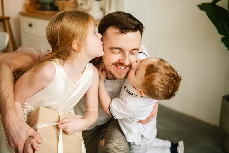 A dad getting kissed on either cheek by his two young children.