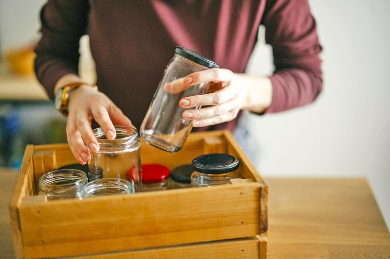 Anonymous man putting clean, empty jars into a wooden crate for storage.
