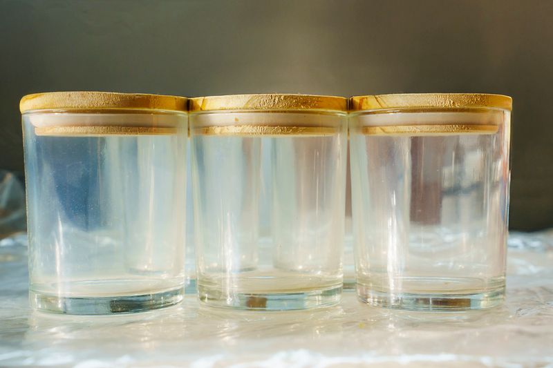 Three identical, empty clear glass candle jars with wooden lids.