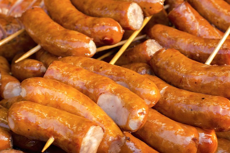 Dozens of grilled sausages on bamboo skewers, stacked on top of each other.