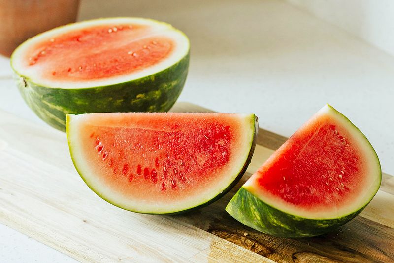 One half of a watermelon and two quarters on a wooden cutting board.