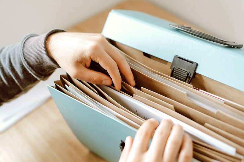 Anonymous person shuffling through files in an accordion file folder.