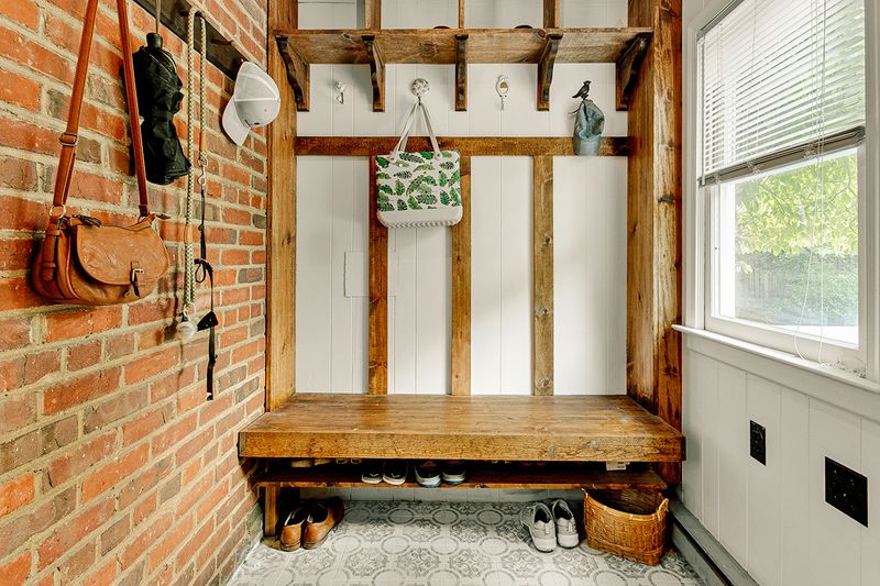 A mudroom in an older home with a wooden bench, lots of hooks, shelves, shoe storage, and several accessories.