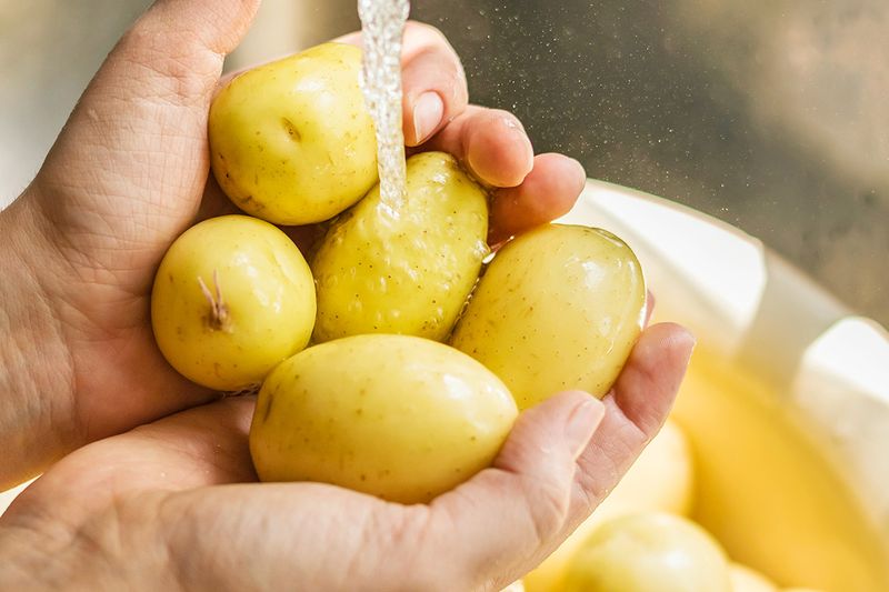 Anonymous person's hands holding small, yellow potatoes under a running tap to clean them.