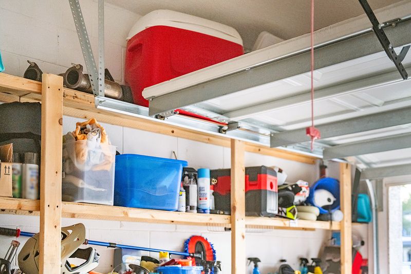 A garage with the door open and wooden storage shelves packed with miscellaneous items.