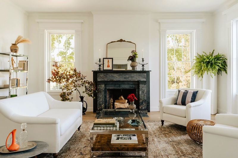 A living room with white walls, white furniture, and a fireplace as the focal point. The accent furniture and decor represent a variety of design styles.