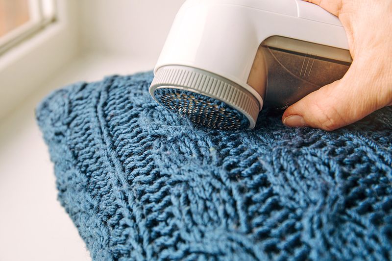 Anonymous person using a fabric shaver on a blue cable knit sweater.