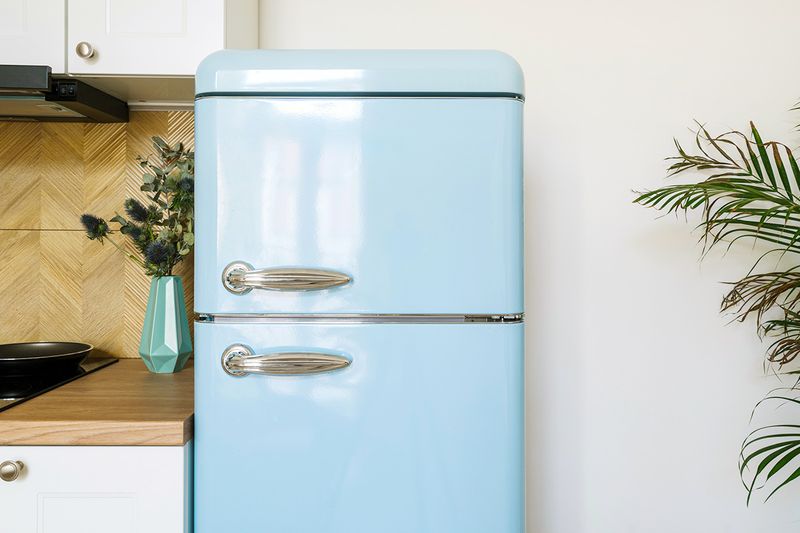 A small, retro-style refrigerator in light blue in a white kitchen with a yellow backsplash and wood countertops.