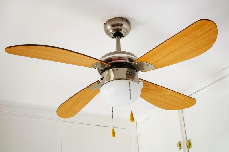 A ceiling fan with a chrome motor housing and wooden blades with pull chains.