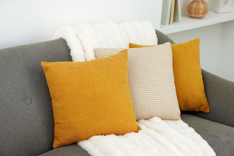 Three pillows in shades of yellow on a dark gray sofa. Two of the pillows are solid color, and the one in the middle has a textured, geometric grid pattern.