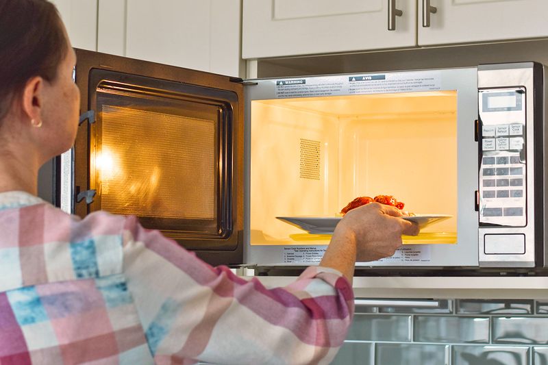Anonymous woman placing a plate of food into a microwave oven.