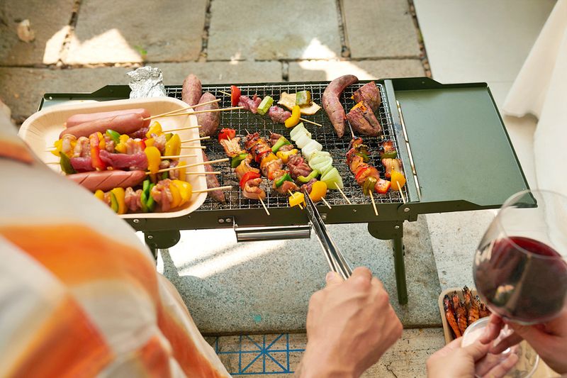 Anonymous person putting various kebabs with meat and veggies on a charcoal grill.