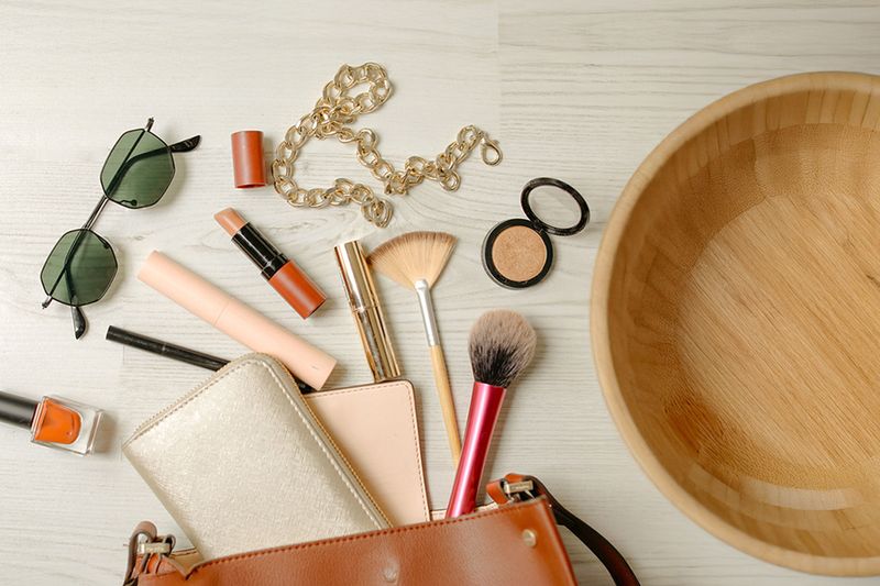 Purse essentials sprawled out on a countertop next to a large wooden bowl.