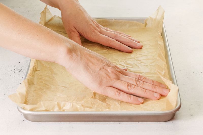 Anonymous person flattening some crumpled up parchment paper onto a sheet pan.