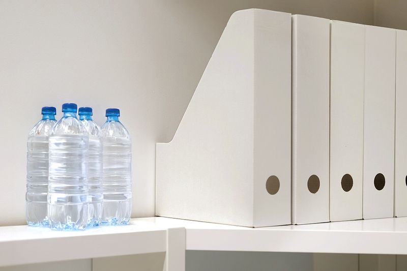 Five white magazine files on a shelf next to four disposable plastic water bottles.