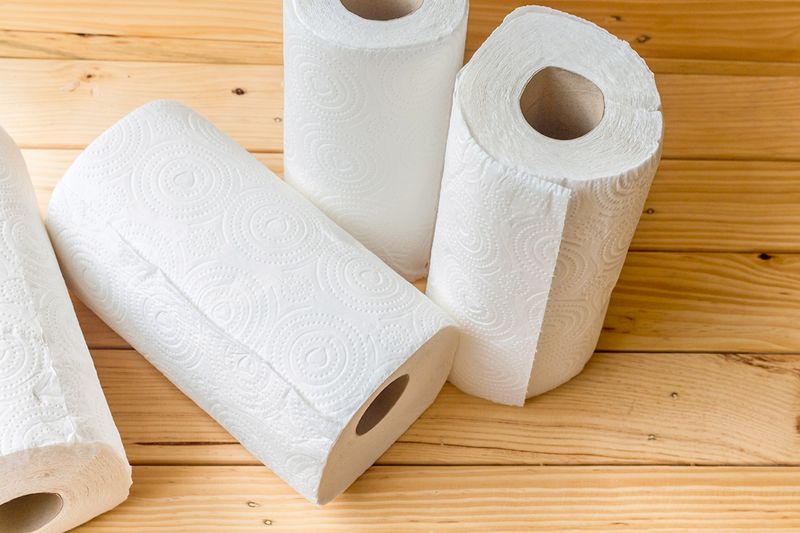 Four rolls of paper towels — two standing upright and two on their sides — on a light wood floor.