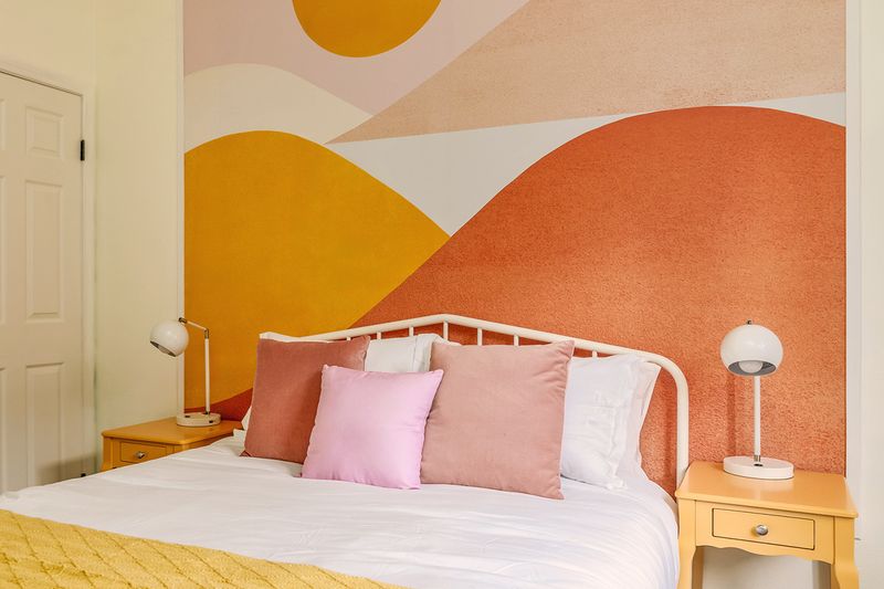 A colorful bedroom with an abstract mural behind the bed that appears to be framed.