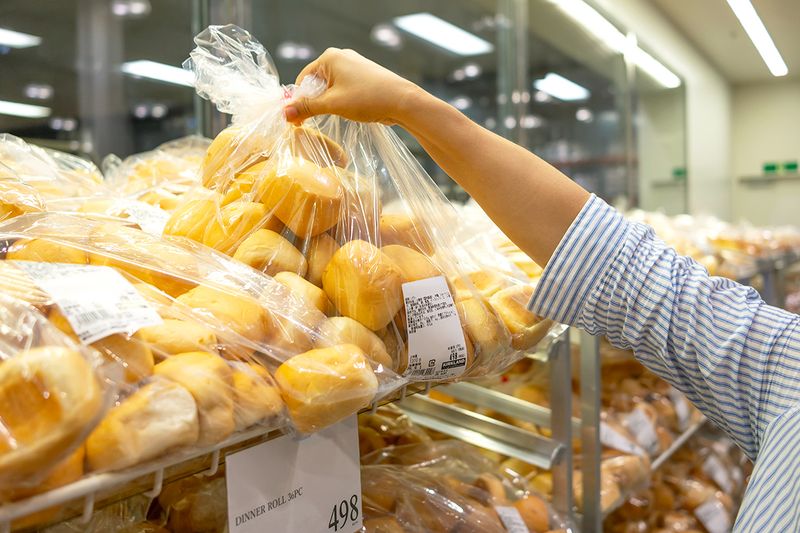 Anonymous woman grabbing a bag of dinner rolls at the Costco bakery.