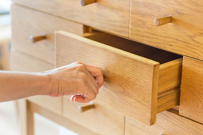Anonymous person's hand opening a drawer in a wooden dresser.