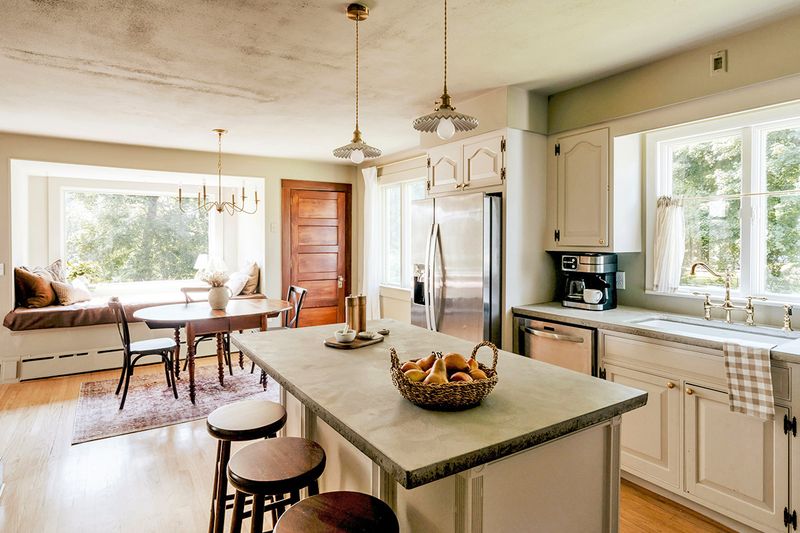An open concept kitchen and dining area. The kitchen cabinets are white, the countertops are concrete, and the floors are pine.