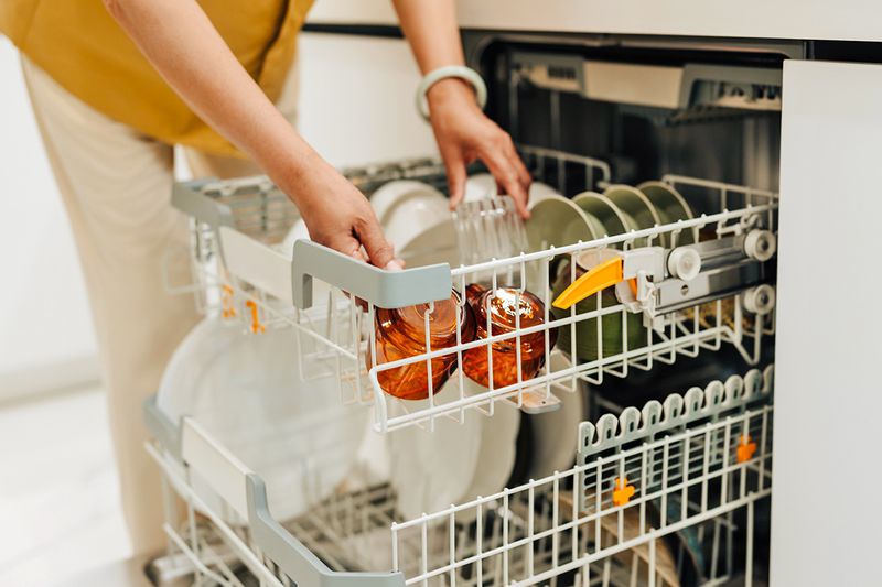 Anonymous person loading the top rack of a dishwasher with coffee mugs.