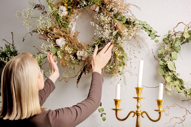 Woman hanging a dried floral wreath on the wall.