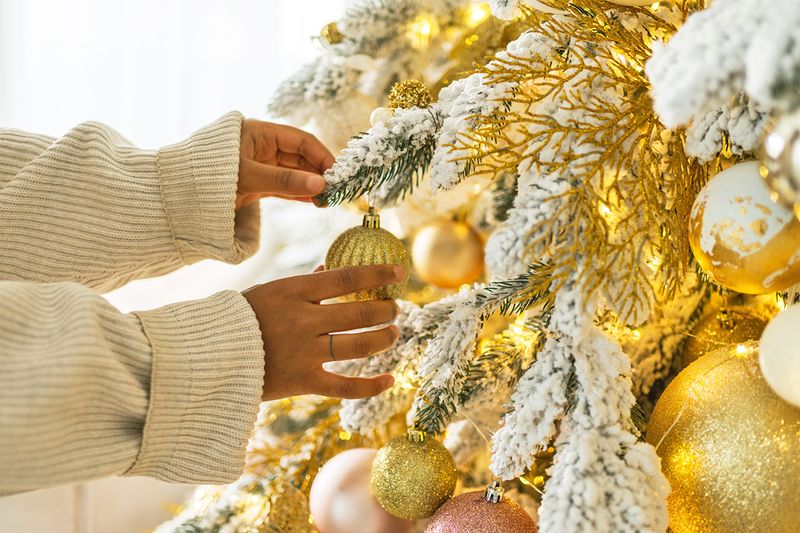 Anonymous woman adjusting a gold glittery ornament on a flocked Christmas tree.