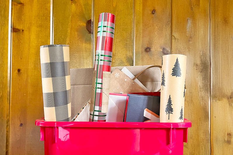 An organizing bin filled with gift wrapping essentials, including wrapping paper rolls, gift bags, and boxes.