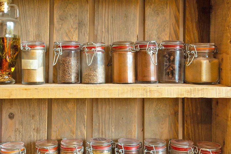Two shelves of spices in airtight glass jars.
