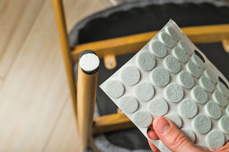 Anonymous person holding a sheet of round, felt furniture protectors. It appears they just applied one to the bottom of a chair leg.