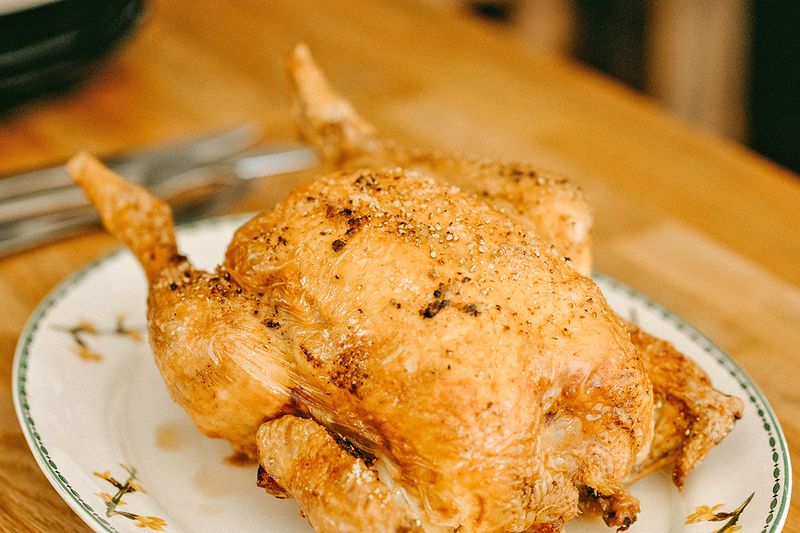 A cooked whole chicken on a patterned ceramic dish.