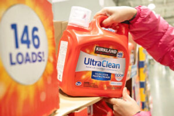 Anonymous person pulling a large bottle of Kirkland Signature Ultra Clean HE Liquid Laundry Detergent off a shelf.
