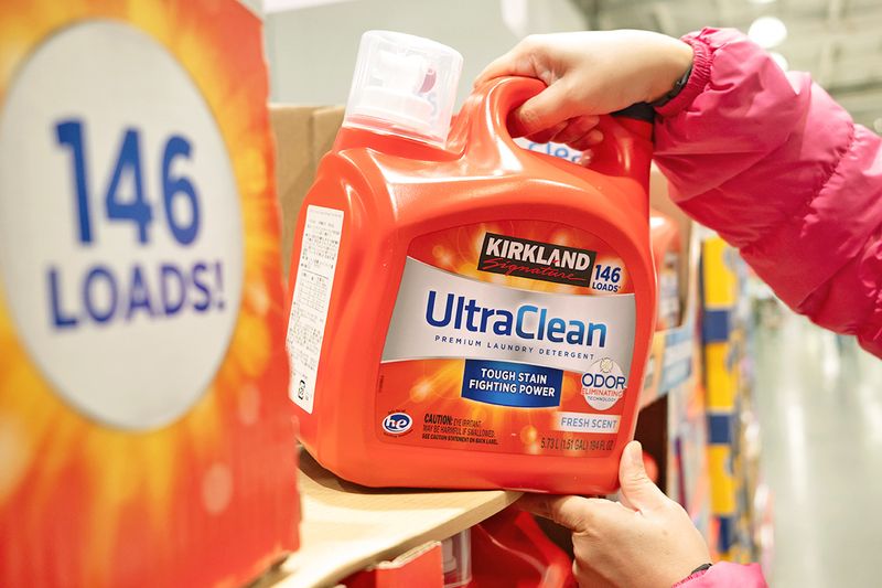 Anonymous person pulling a large bottle of Kirkland Signature Ultra Clean HE Liquid Laundry Detergent off a shelf.