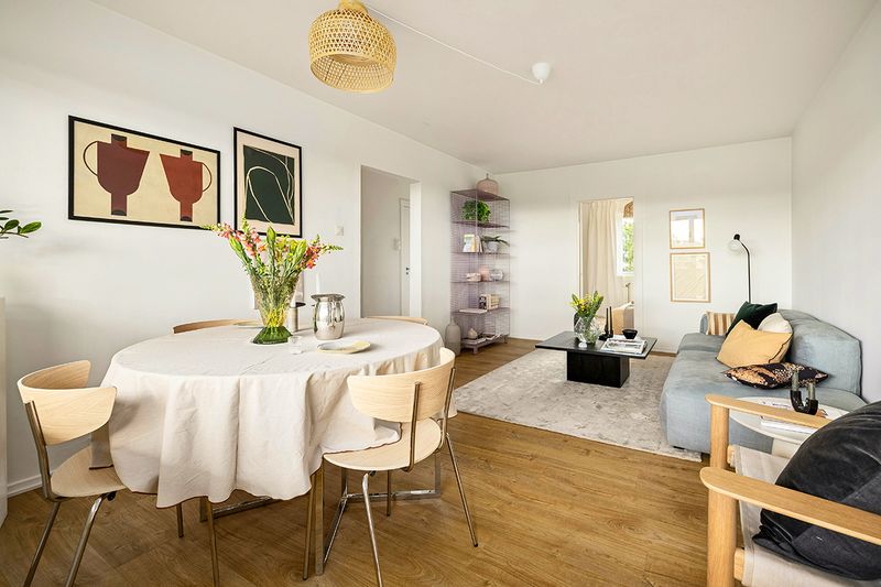 A modern, open concept living and dining area in an apartment. There's lots of art, fresh flowers, and wood tones.