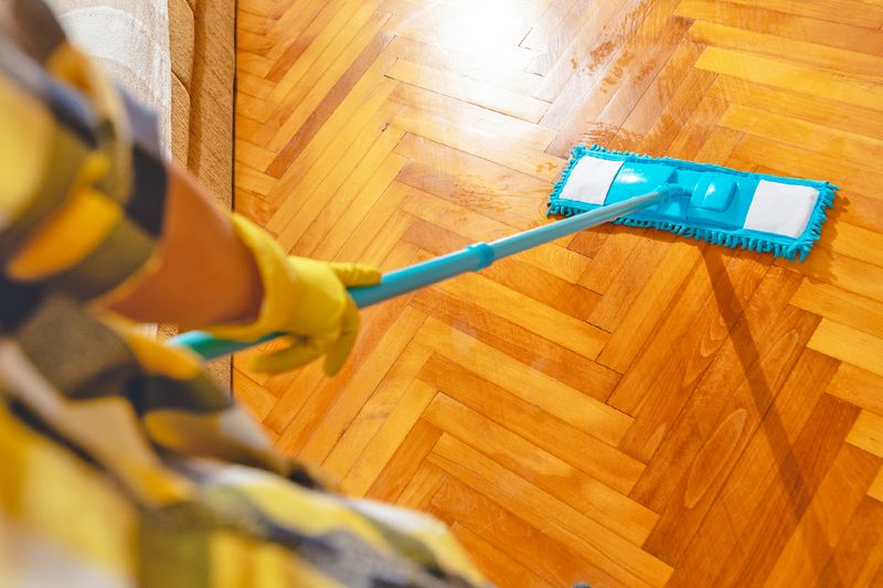 Anonymous person cleaning wood floors in a herringbone pattern with a flat mop.