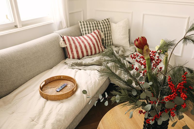 A light gray sofa with a round woven tray on it. Inside the tray is a remote.