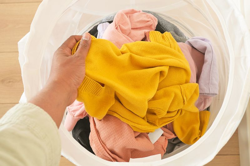 Anonymous person reaching into a laundry hamper full of colorful clothing.