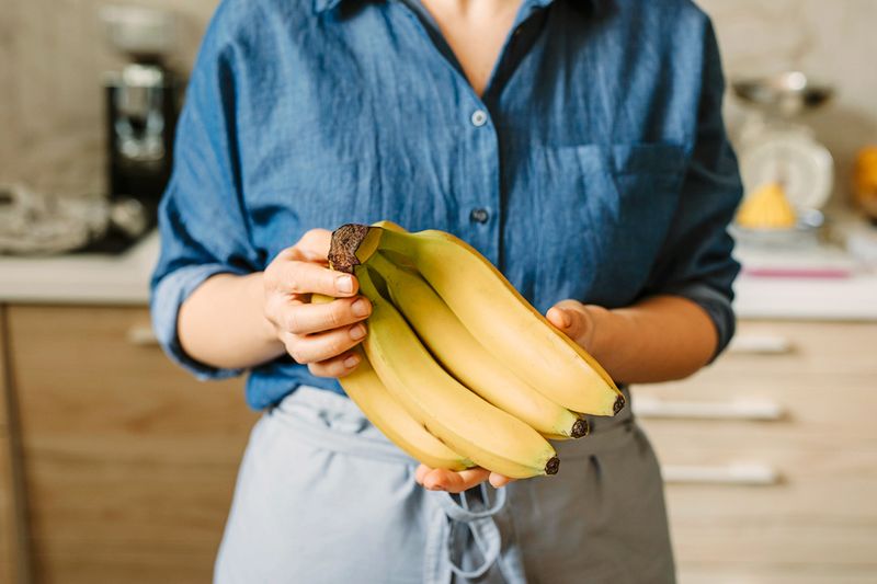 Anonymous woman holding a bunch of yellow bananas.