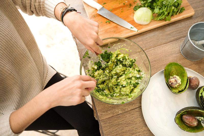 Anonymous woman making guacamole in a glass bowl using two forks.