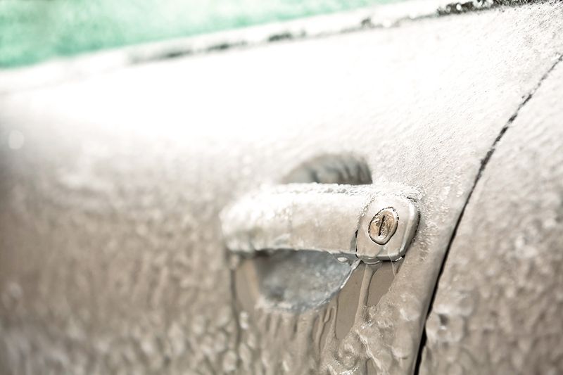 A close-up of a car door covered in ice from freezing weather.
