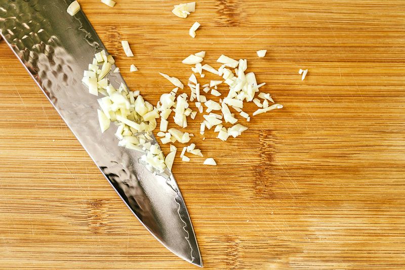 Chopped garlic on a wooden cutting board next to a chef's knife.