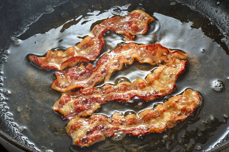 Close up of sizzling bacon frying in its own fat inside a skillet.