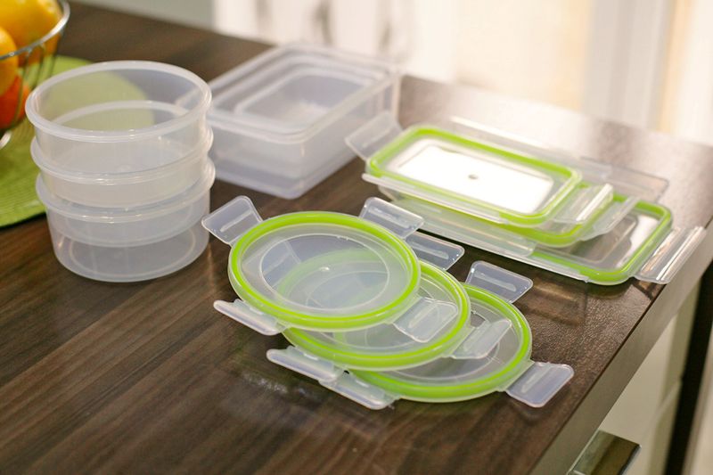 A collection of empty plastic food storage containers, separated into lids and containers, on a wooden table.
