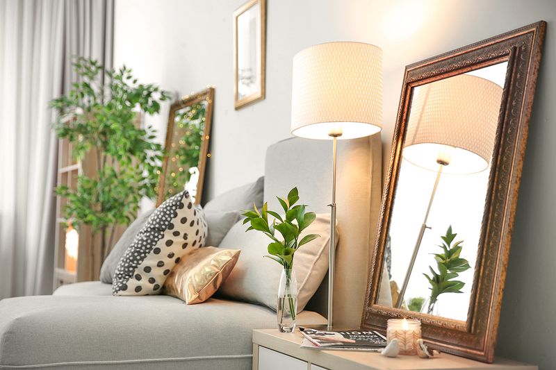 A nightstand with a mirror leaning against the wall and a small table lamp in front of it.